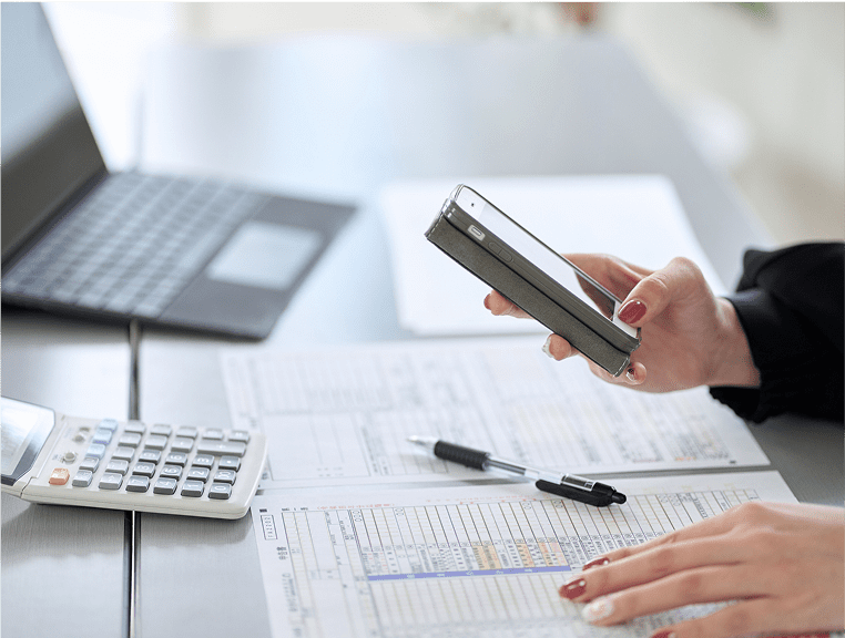 A person using their cell phone on top of papers.