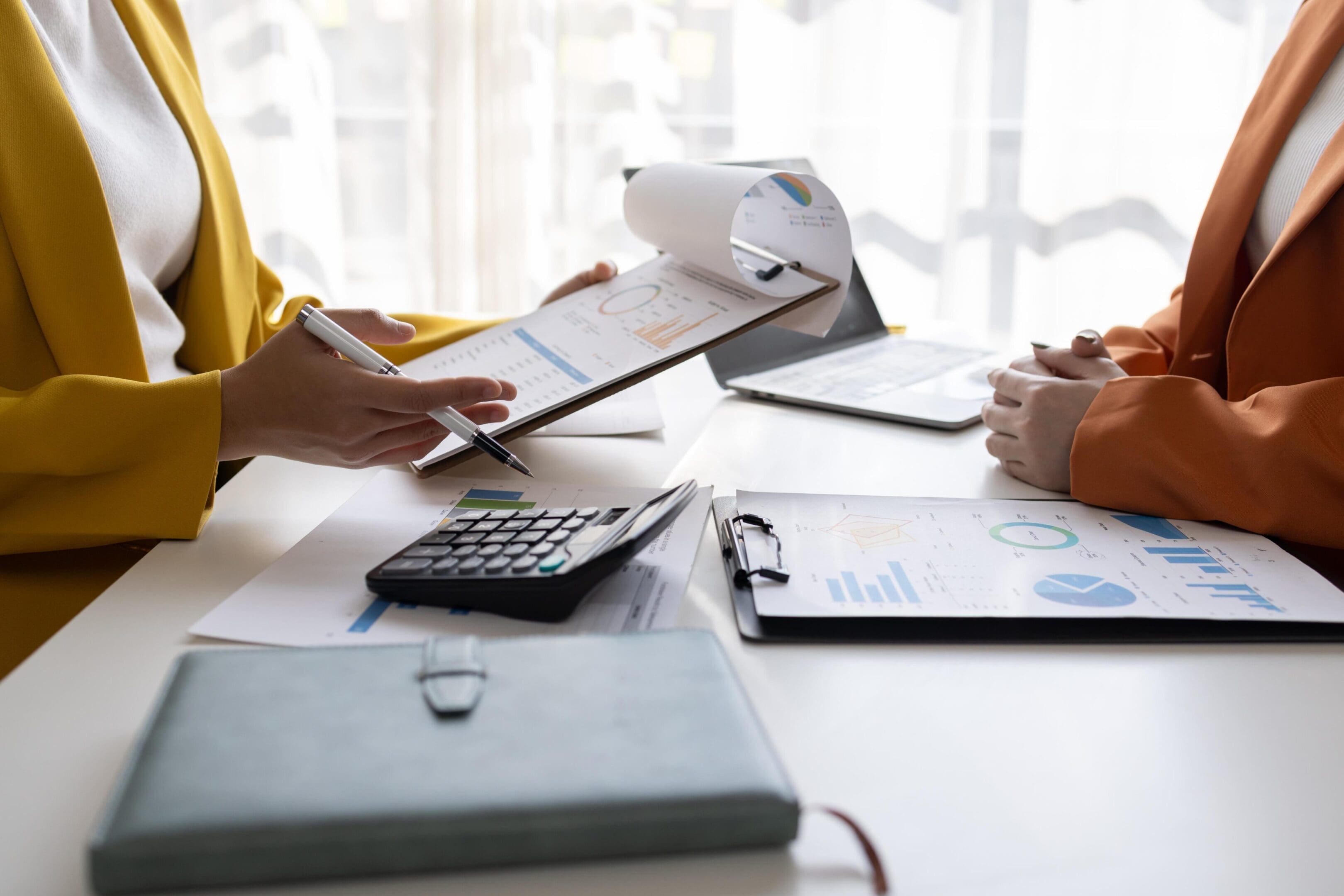 Two people reviewing financial documents with calculator and laptop.